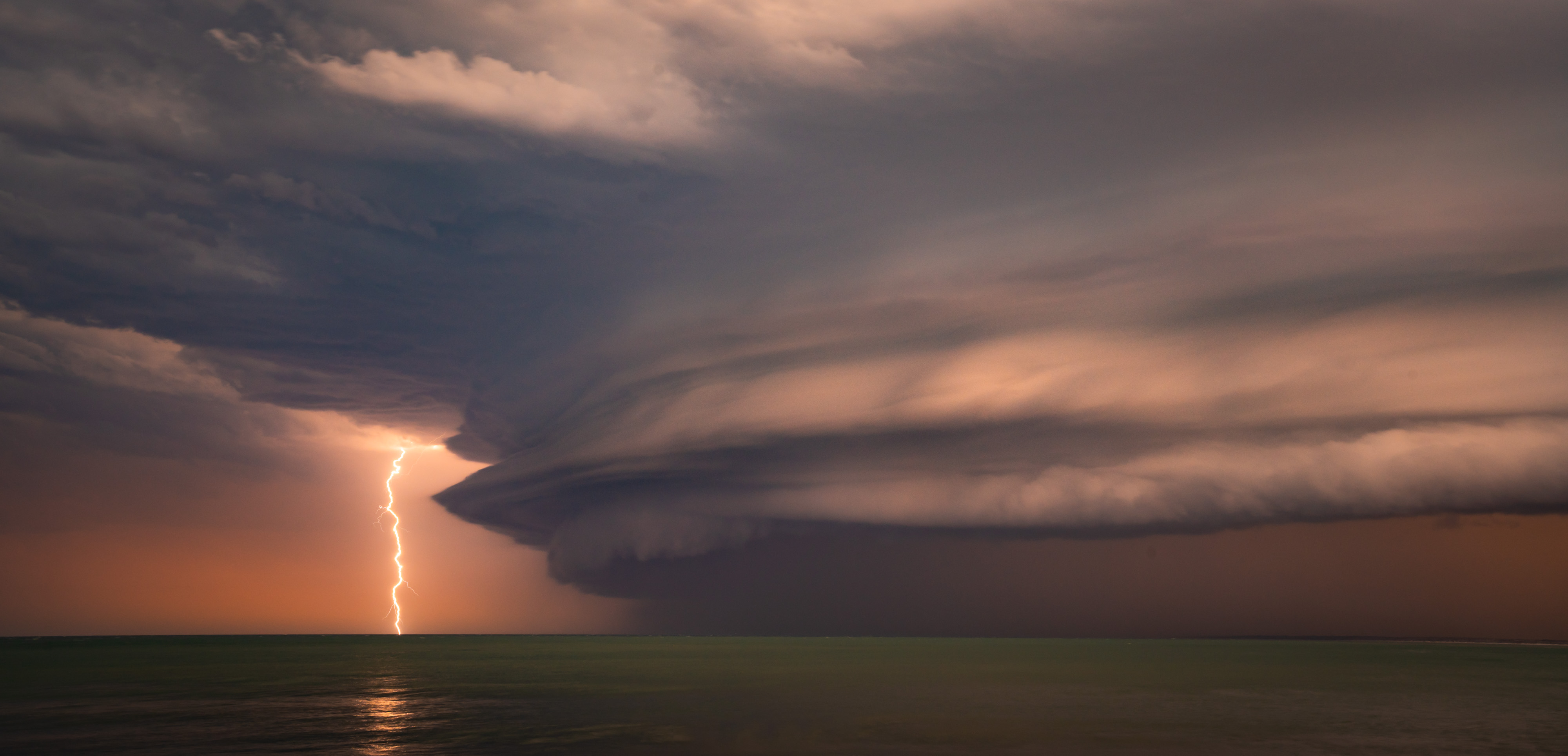 A lightning strike in the distance against a peach coloured storm clouds
