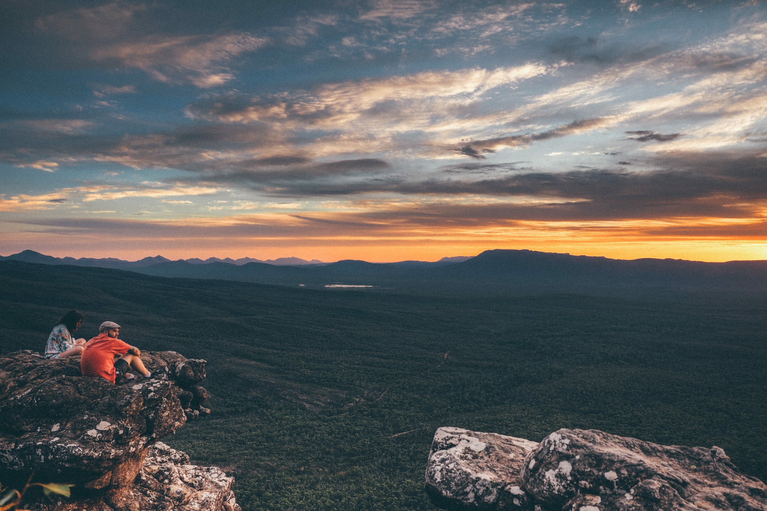 hikers on a ledge looking at a sunset